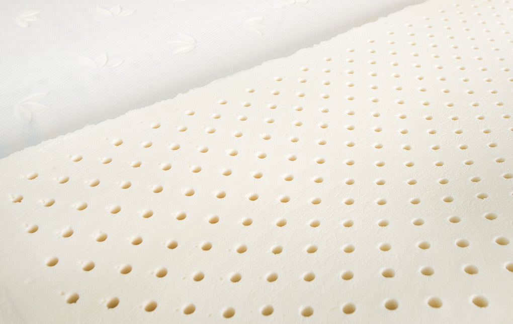 A close-up of a perforated natural latex mattress core with a quilted cover peeled back, highlighting its breathable design for comfort